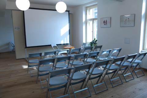 Fotografie sdíleného prostoru se židlemi v divadelním uspořádání, pohled z šatny